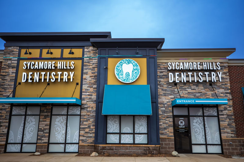 Exterior view of Sycamore Hills Dentistry with signage and entrance, showcasing a modern dental office building with stone facade and blue accents.