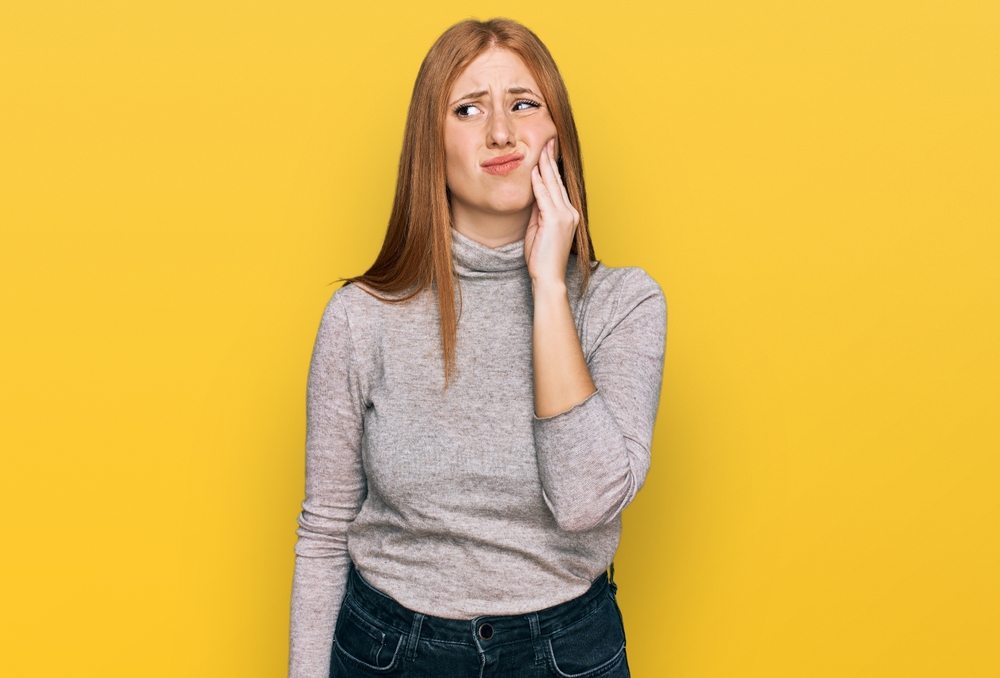 woman holding mouth in pain against cheerful yellow background